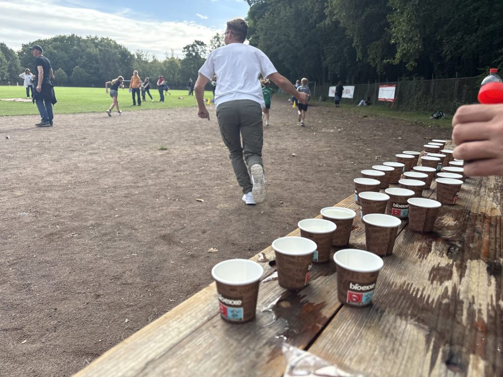 Ein Vater läuft mit einem Becher Wasser zu seiner laufenden Tochter
